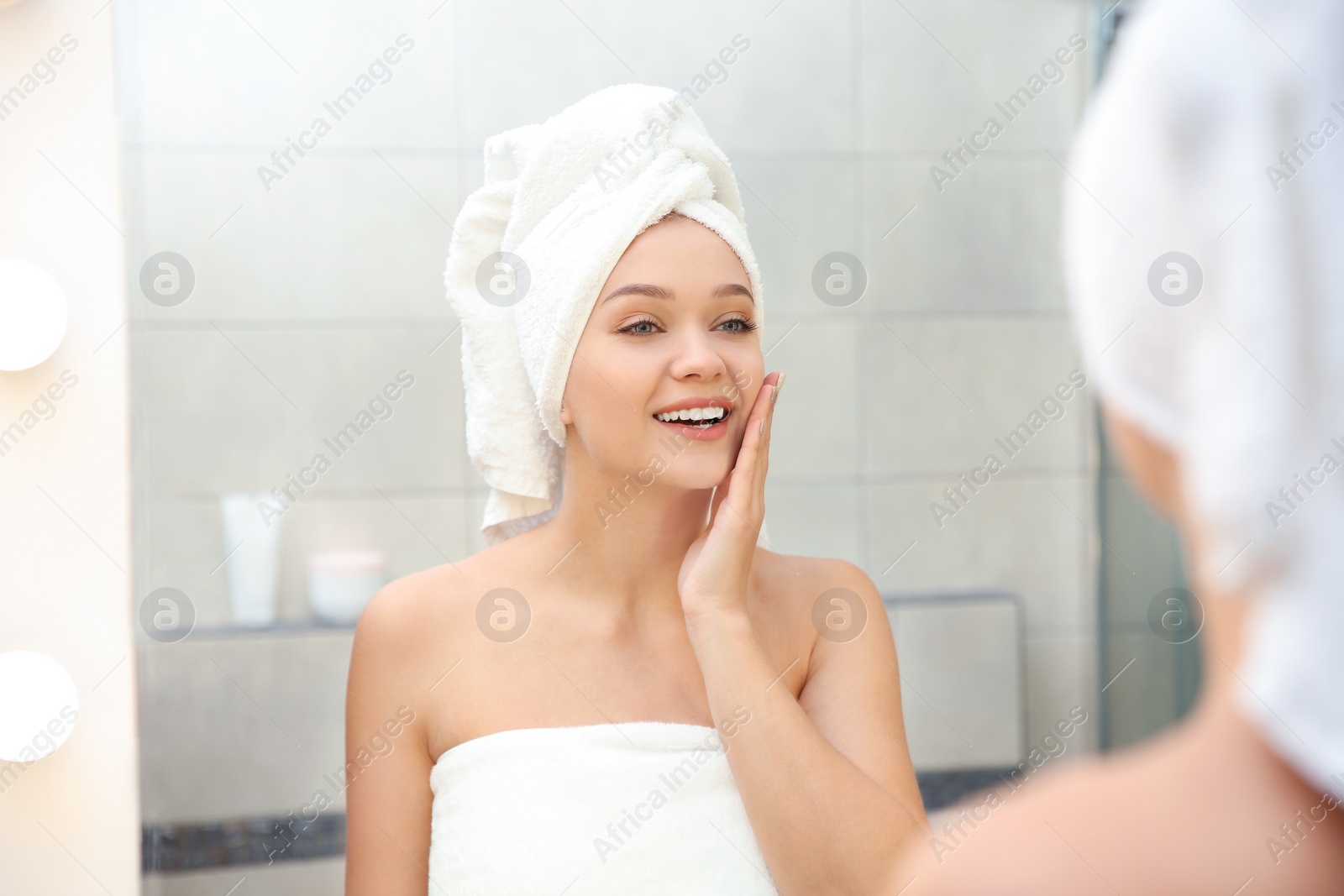 Photo of Beautiful woman with clean towels near mirror in bathroom