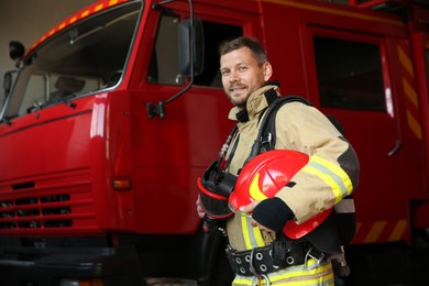 Photo of Firefighter in uniform with helmet near red fire truck at station