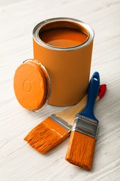 Photo of Can of orange paint and brushes on white wooden table