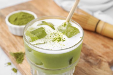 Photo of Glass of tasty iced matcha latte on wooden board, closeup