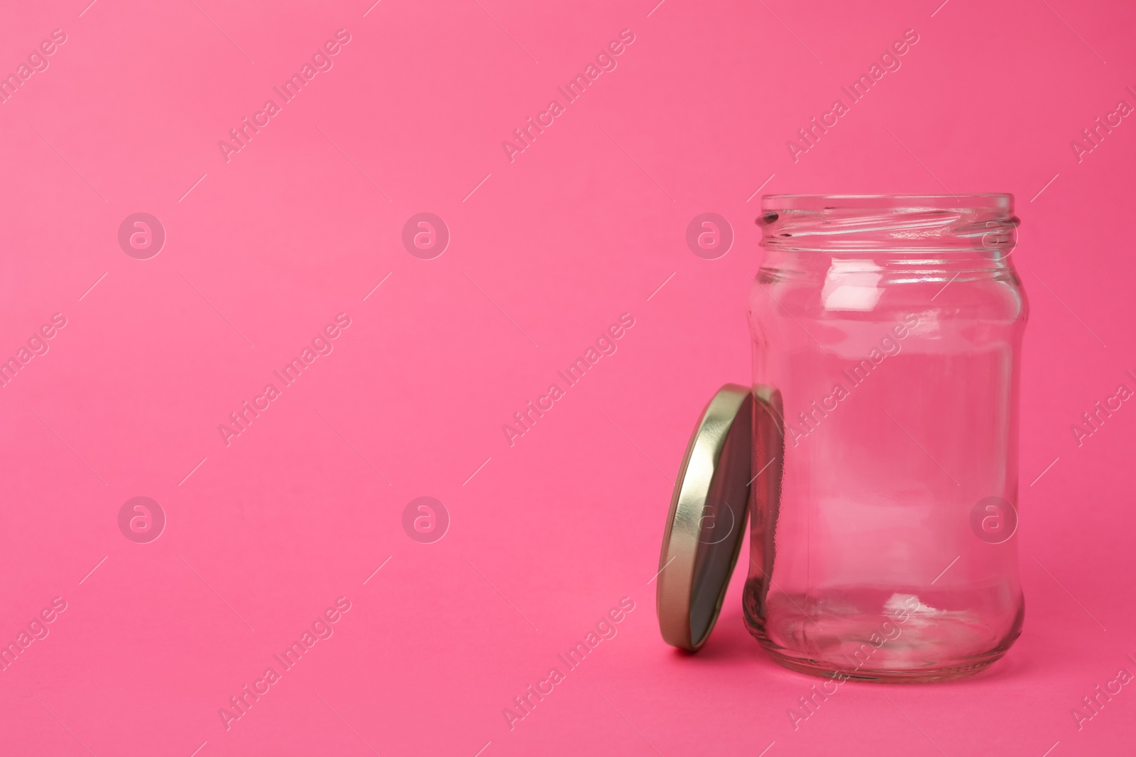 Photo of Open empty glass jar on pink background, space for text