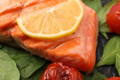 Photo of Tasty grilled salmon with lemon, spinach and tomatoes on table, closeup