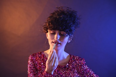 Photo of Beautiful young woman with lipstick posing on color background in neon lights