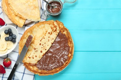 Tasty crepes with chocolate paste and berries served on turquoise wooden table, flat lay. Space for text