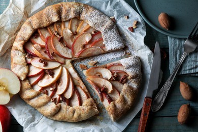 Delicious apple galette with pecans and knife on wooden table, flat lay
