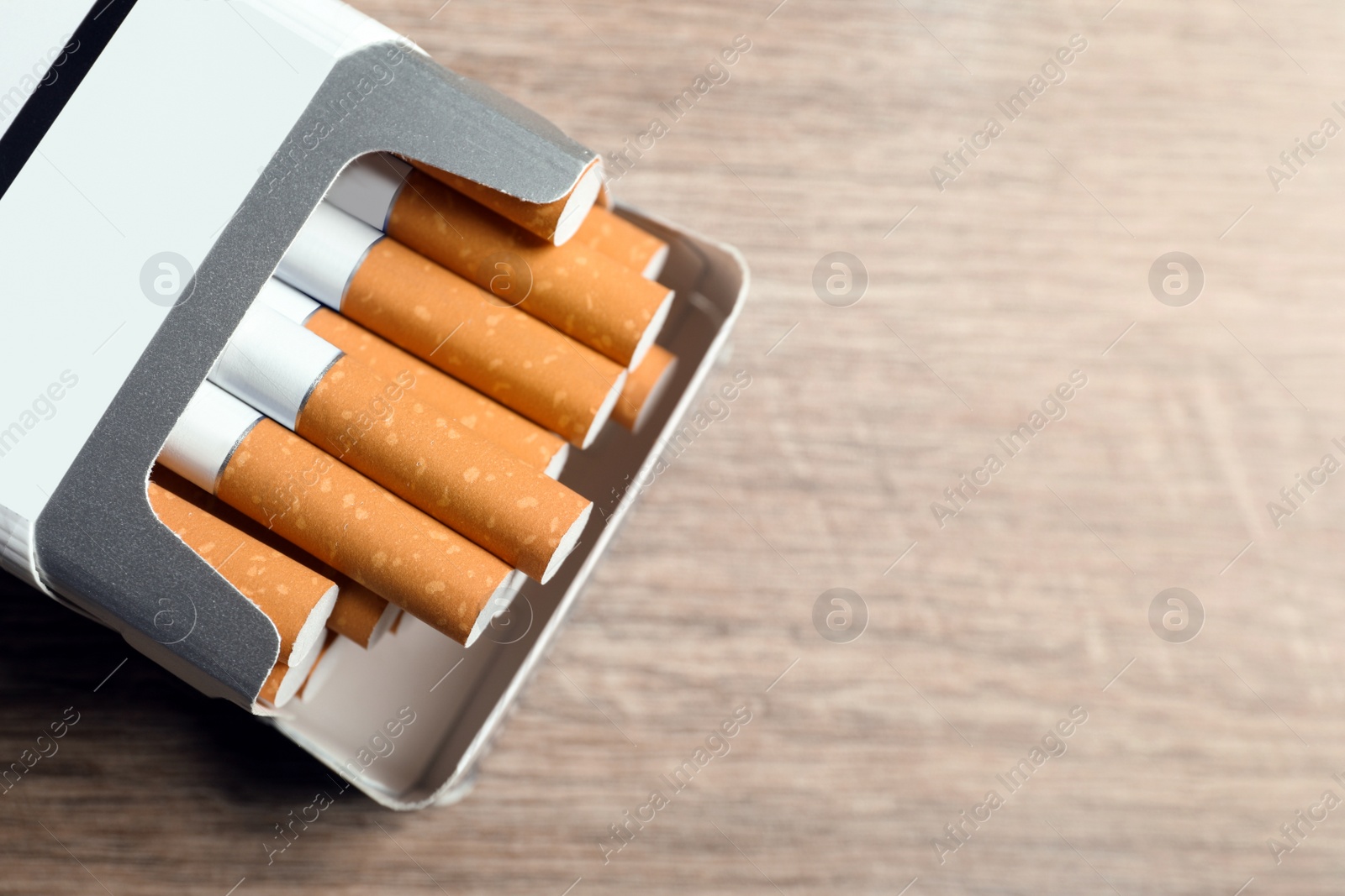 Photo of Cigarettes in pack on wooden table, top view. Space for text