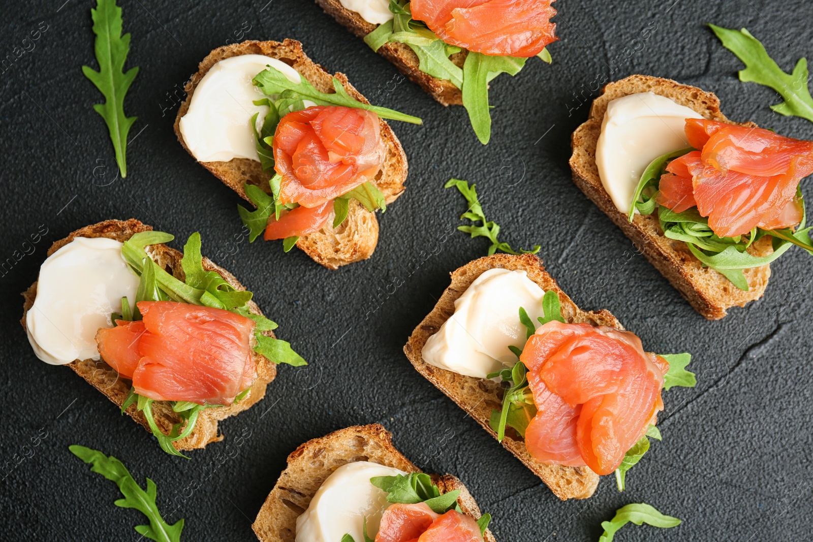 Photo of Tasty sandwiches with fresh sliced salmon fillet on dark background, top view