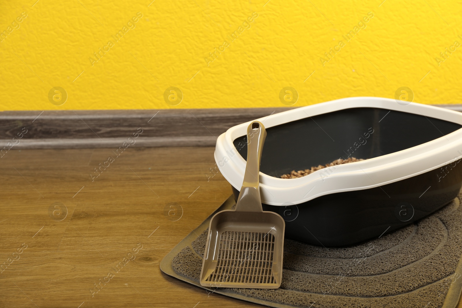 Photo of Cat tray with biodegradable litter and scoop on floor near yellow wall. Space for text