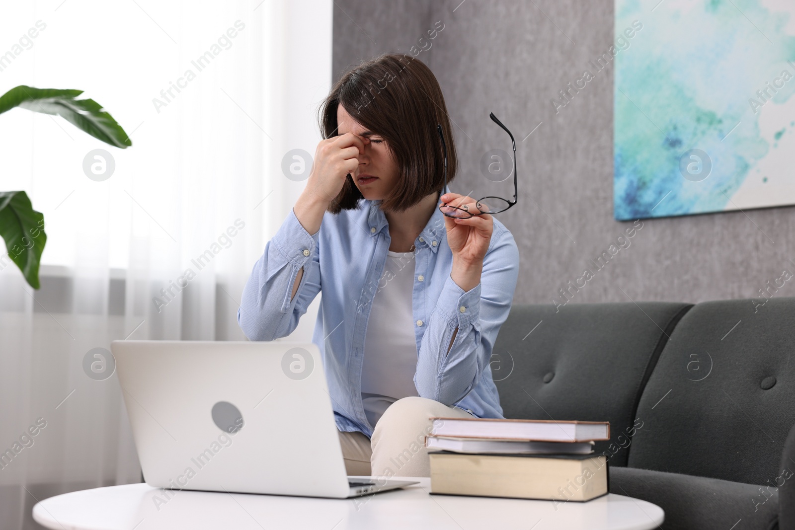 Photo of Overwhelmed woman with glasses sitting on sofa indoors