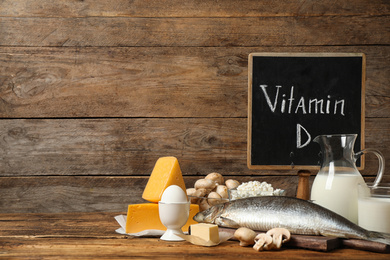Photo of Chalkboard with phrase VITAMIN D and fresh products on wooden table