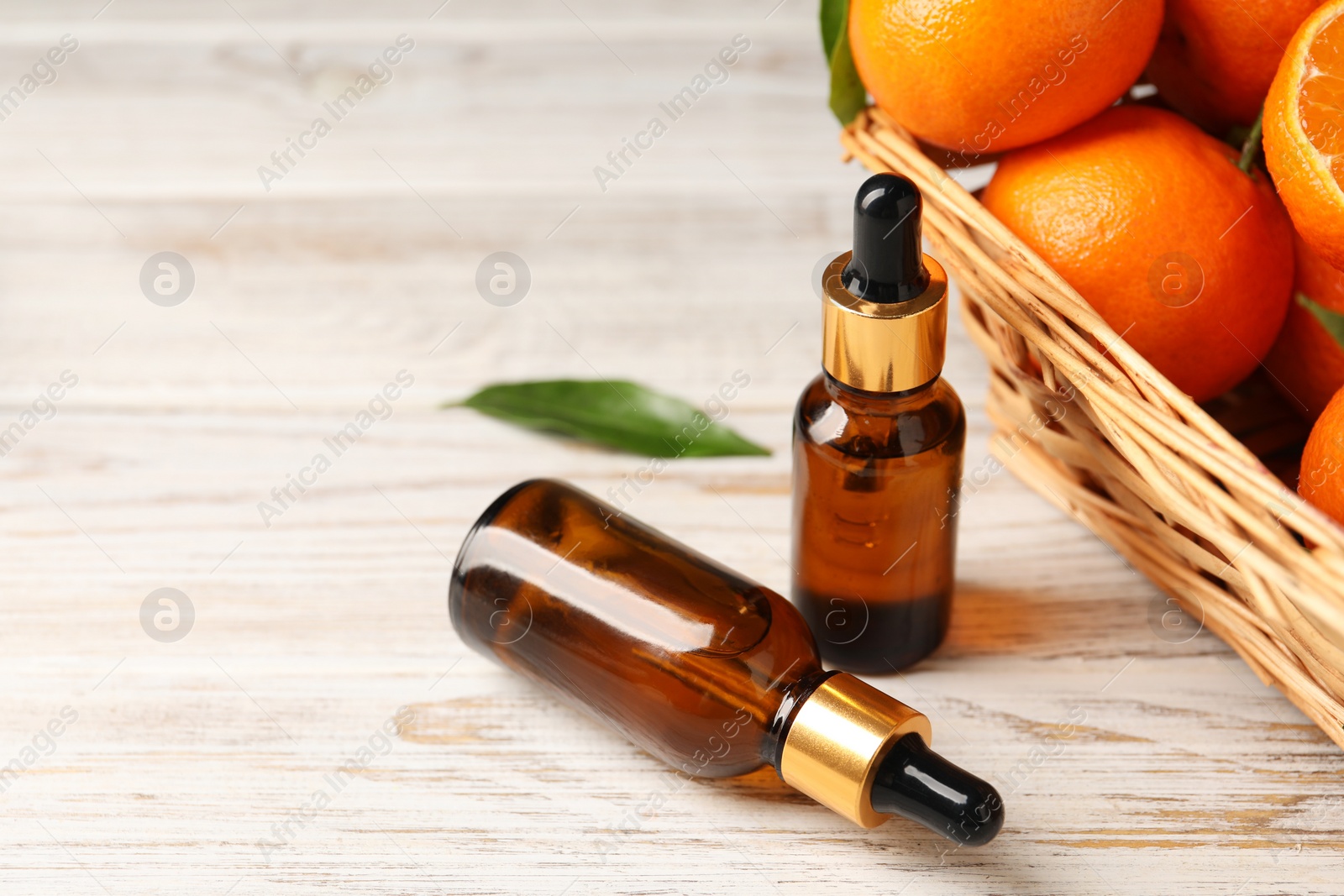 Photo of Bottle of tangerine essential oil and fresh fruits on white wooden table