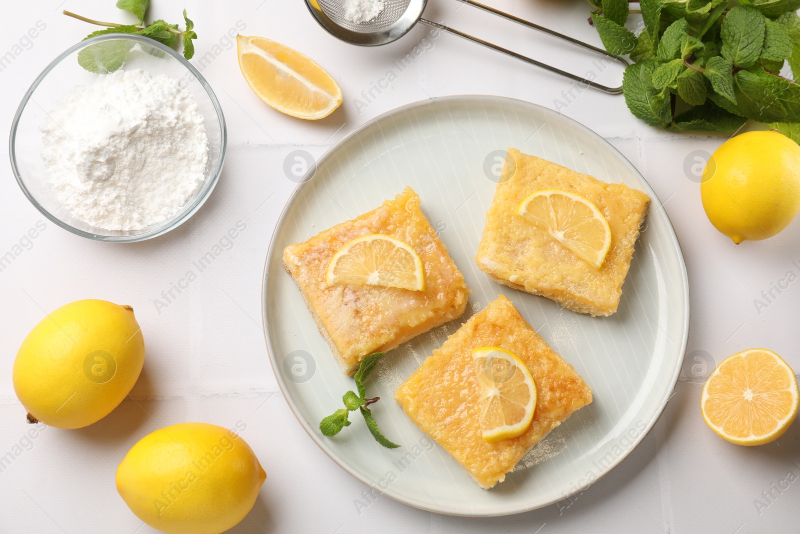 Photo of Tasty lemon bars and mint on white tiled table, flat lay