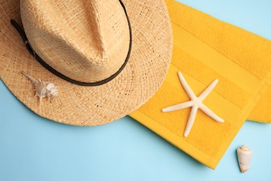 Straw hat, towel, starfish and shells on light blue background, flat lay. Beach accessories