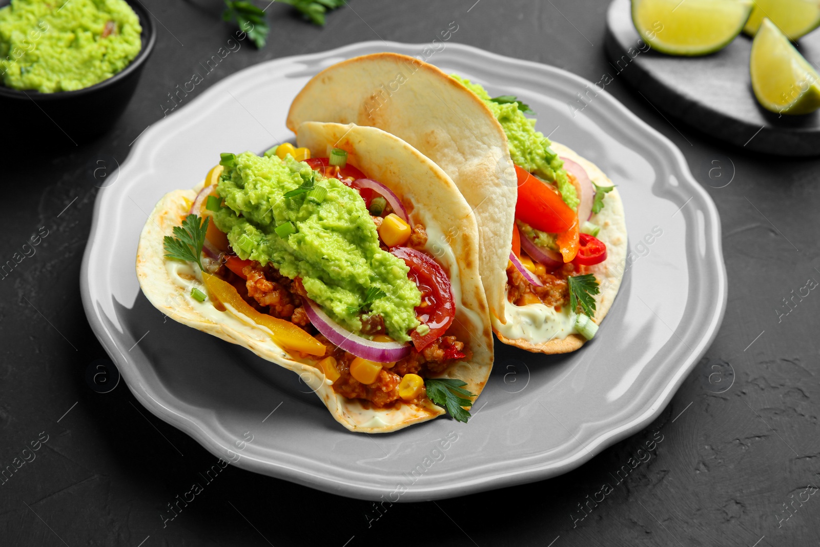 Photo of Delicious tacos with guacamole, meat and vegetables on black table, closeup