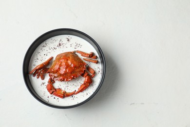 Photo of Delicious boiled crab with cream sauce in bowl on white table, top view. Space for text