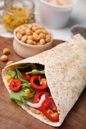 Photo of Delicious hummus wrap with vegetables on wooden board, closeup