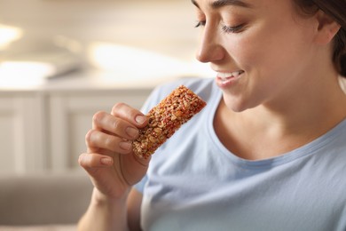 Photo of Woman eating tasty granola bar at home, closeup