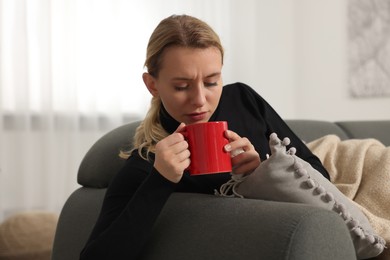 Photo of Sick woman with tissue and cup of drink on sofa at home. Cold symptoms