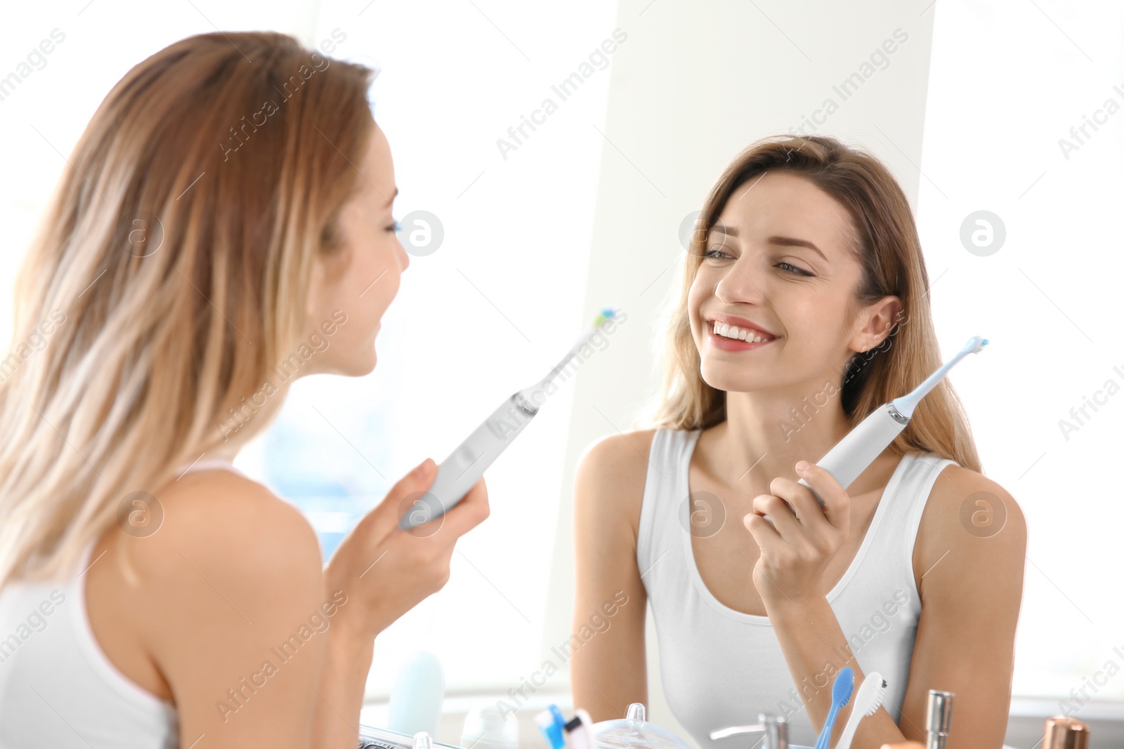 Photo of Young beautiful woman with toothbrush near mirror in bathroom. Personal hygiene