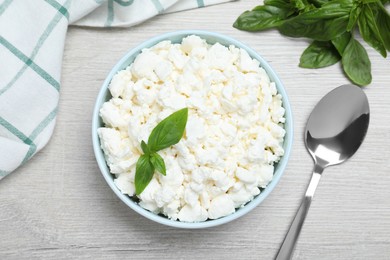 Photo of Fresh cottage cheese with basil in bowl on light wooden table, flat lay