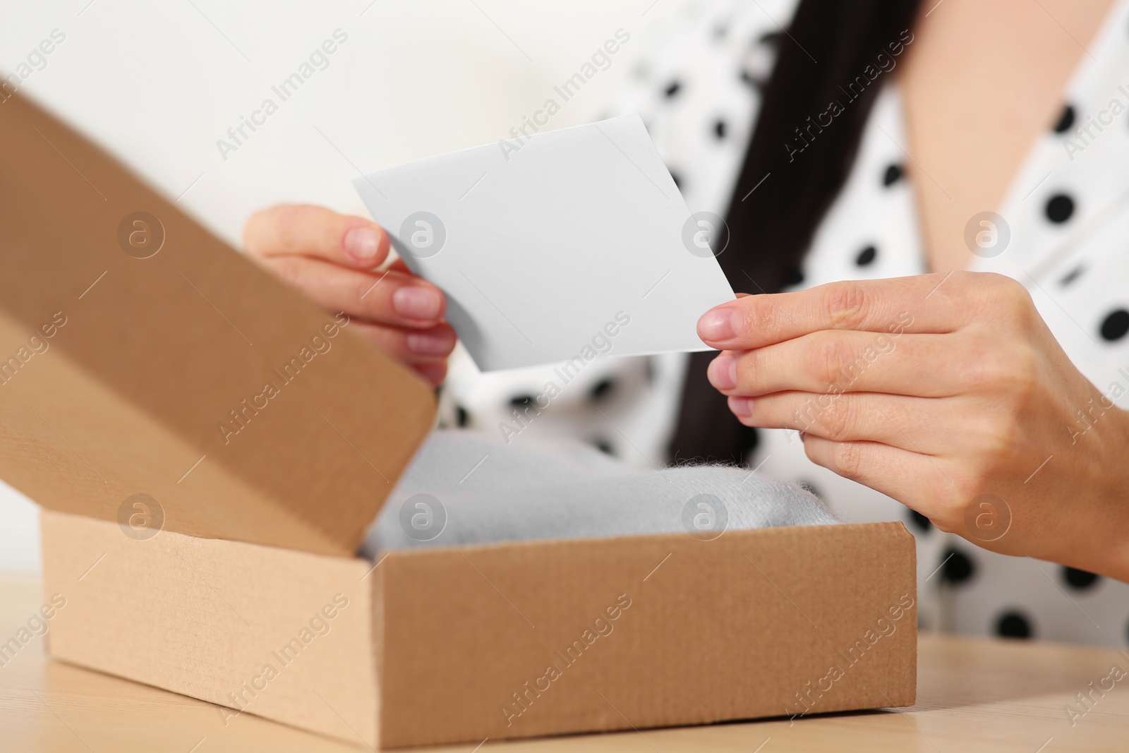 Photo of Woman holding greeting card near parcel with Christmas gift, closeup