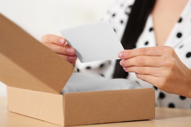 Woman holding greeting card near parcel with Christmas gift, closeup