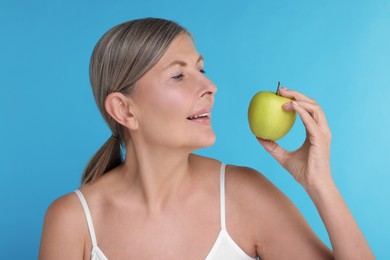 Beautiful woman with fresh apple on light blue background. Vitamin rich food