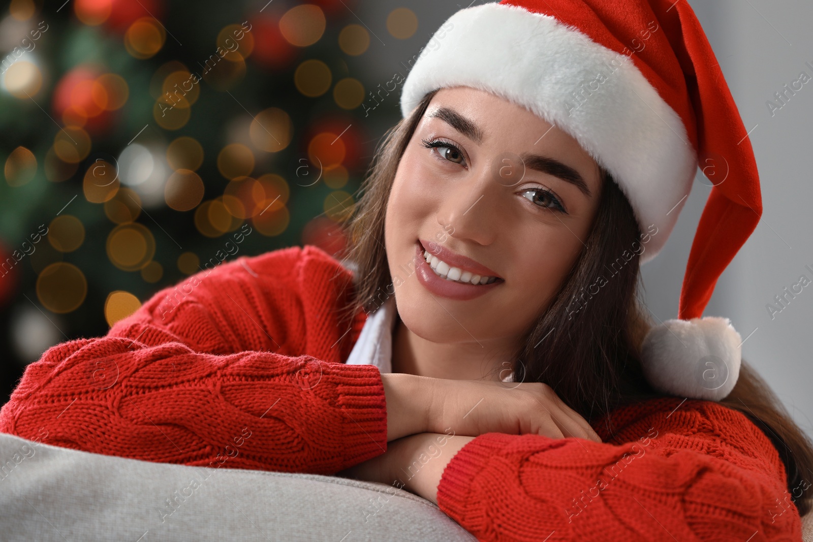 Photo of Smiling woman wearing red Santa hat near Christmas tree