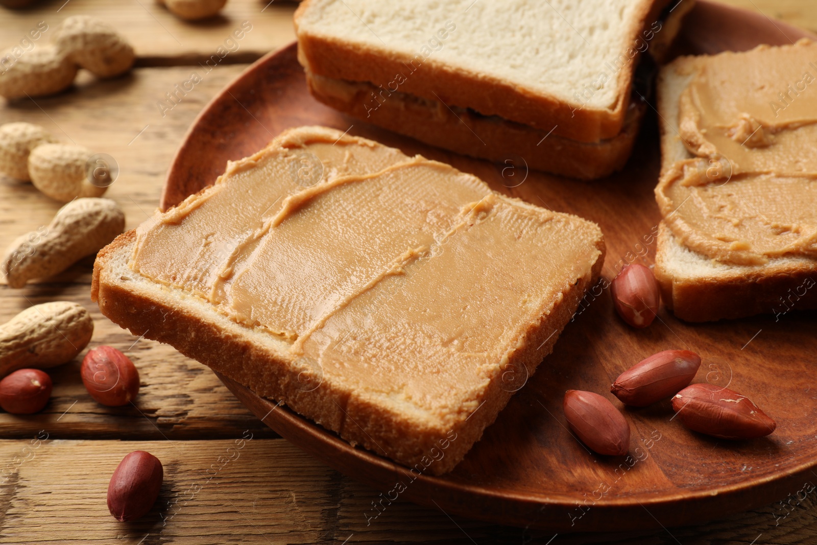 Photo of Tasty peanut butter sandwiches and peanuts on wooden table, closeup