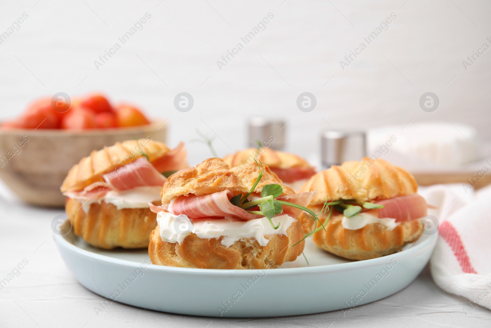 Photo of Delicious profiteroles with cream cheese and prosciutto on white table, closeup