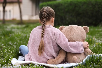 Little girl with teddy bear on plaid outdoors, back view