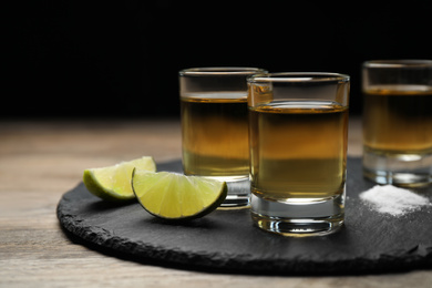 Photo of Mexican Tequila shots, lime slices and salt on wooden table