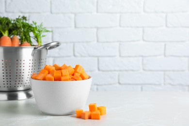 Photo of Bowl of fresh diced carrots on marble table. Space for text