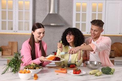 Photo of Friends cooking healthy vegetarian meal at white marble table in kitchen