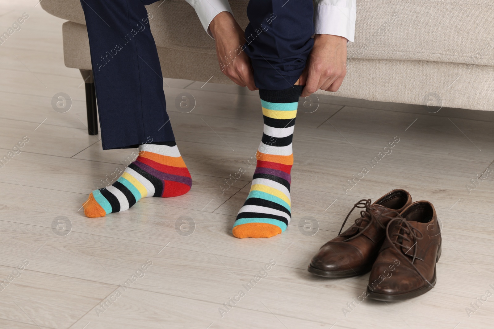 Photo of Man putting on colorful socks indoors, closeup