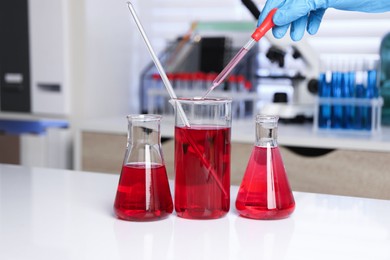 Photo of Laboratory analysis. Woman dripping red liquid into beaker on white table, closeup