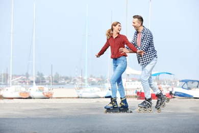 Happy lovely couple roller skating on embankment. Space for text