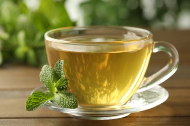 Photo of Glass cup of aromatic green tea with fresh mint on wooden table against blurred background, closeup