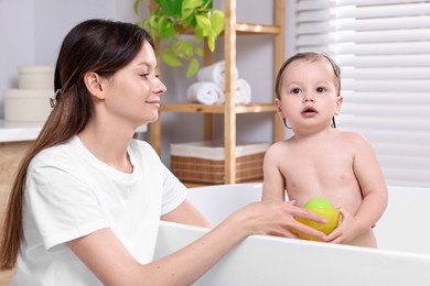 Photo of Mother bathing her cute little baby in tub at home