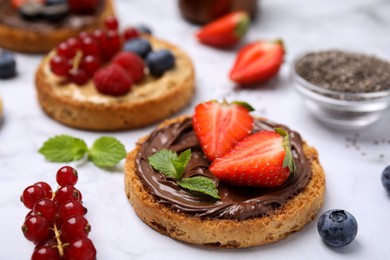 Photo of Tasty organic rusks with different toppings and ingredients on white table, closeup