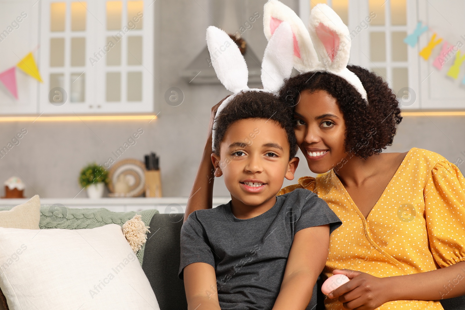 Photo of Happy African American mother and her cute son in bunny ears headband indoors. Easter celebration