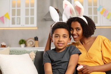 Photo of Happy African American mother and her cute son in bunny ears headband indoors. Easter celebration