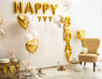 Photo of Phrase HAPPY BIRTHDAY made of golden balloon letters in decorated room