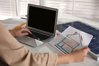 Photo of Woman working on house project with solar panels at table in office, closeup