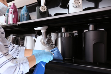 Photo of Woman cleaning shelf with rag and detergent in electronic store, closeup