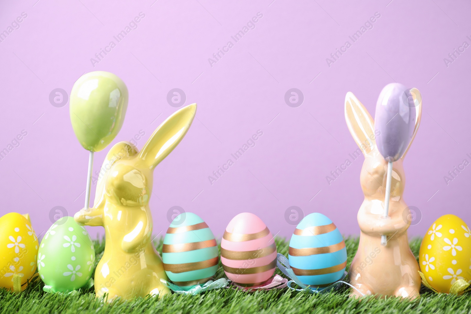 Photo of Easter bunny figures and dyed eggs on green grass against violet background