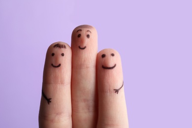 Photo of Three fingers with drawings of happy faces on violet background