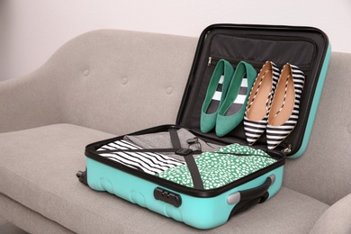 Modern suitcase with clothes and shoes on sofa indoors