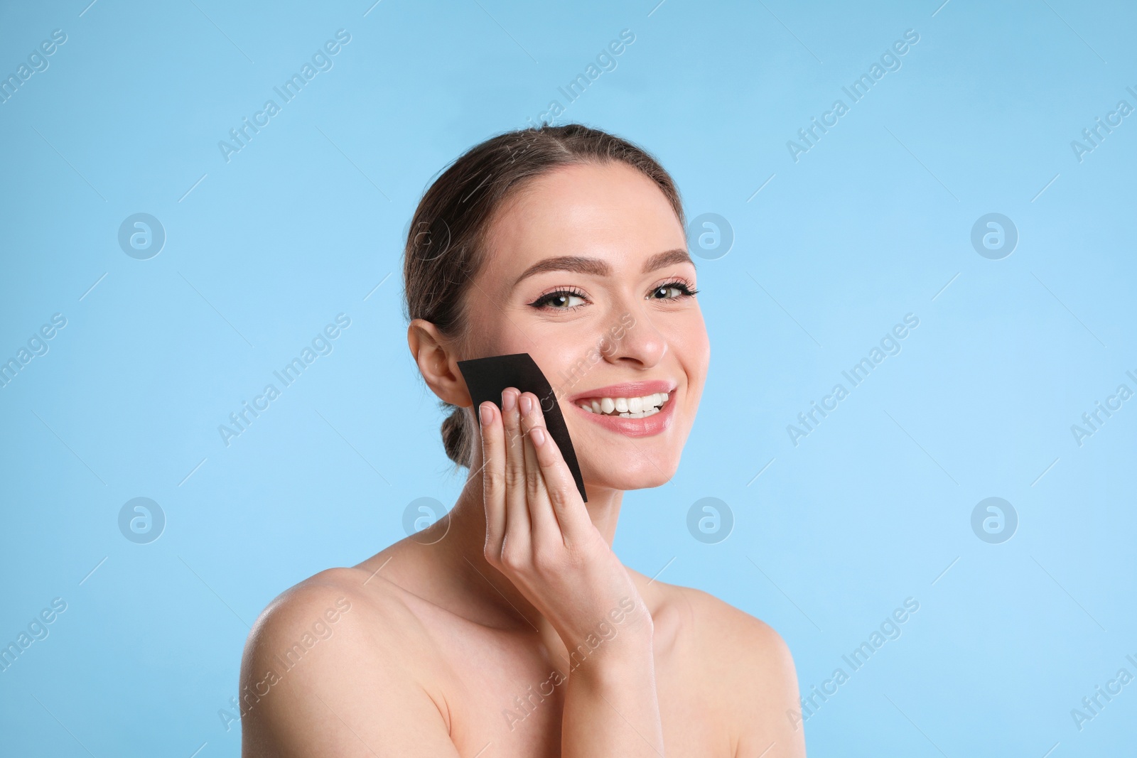 Photo of Beautiful woman using mattifying wipe on light blue background