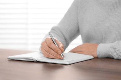 Man writing in notebook at wooden table indoors, closeup